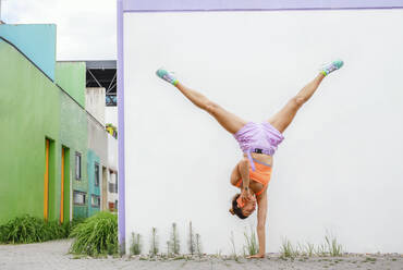 Woman talking on mobile phone while doing handstand in front of wall - AANF00034