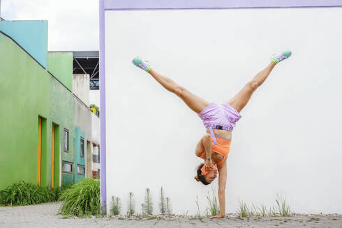 Woman talking on mobile phone while doing handstand in front of wall - AANF00034