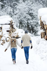 Junges Paar hält sich an den Händen, während es im Schnee spazieren geht - HHF05671