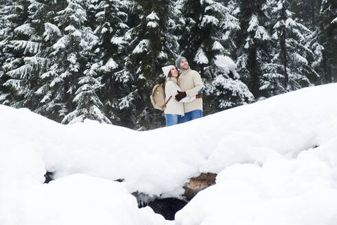 Girlfriend embracing boyfriend in forest during snow - HHF05673