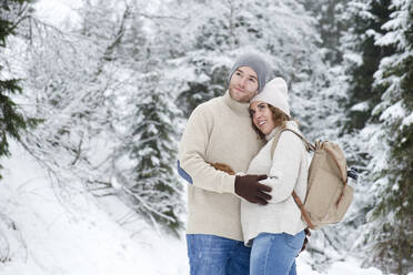Couple embracing while standing in forest during winter - HHF05674