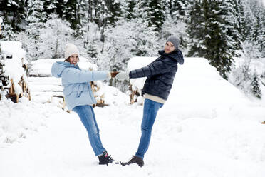 Verspieltes junges Paar hält Hände im Schnee - HHF05676