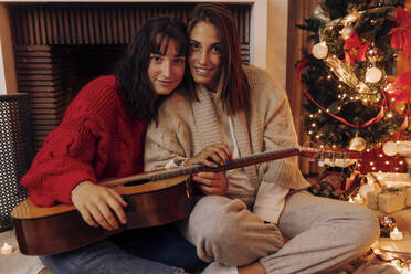 Frau mit Gitarre, die bei einer Freundin zu Hause sitzt, während Weihnachten - EGHF00175