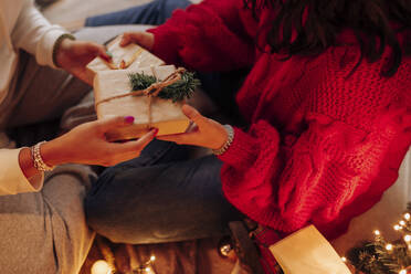 Female friends giving Christmas present at home - EGHF00180