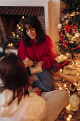 Smiling woman giving Christmas present to female friend at home - EGHF00182