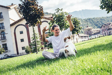 Junger Mann spielt mit Hund, während er auf dem Rasen sitzt - OMIF00038