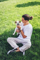 Mid adult man sitting with pet dog on grass - OMIF00042