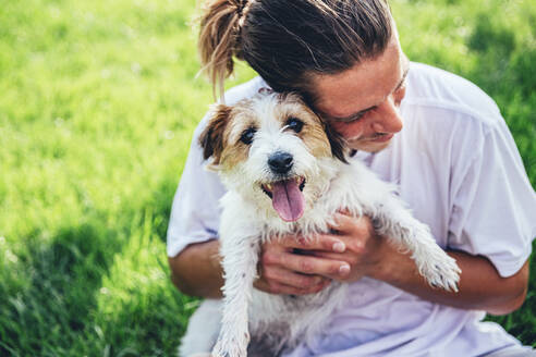 Mittlerer erwachsener Mann umarmt Hund im Rasen - OMIF00043