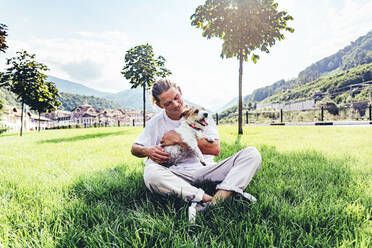 Mid adult man with pet dog sitting cross-legged on grass - OMIF00046