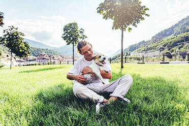 Mittlerer erwachsener Mann mit Hund im Schneidersitz im Gras sitzend - OMIF00046