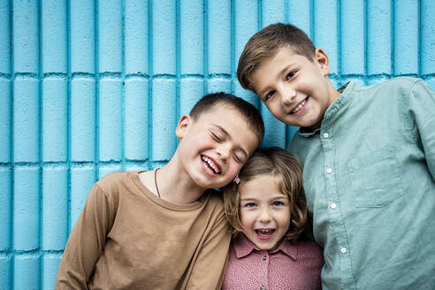 Glückliches Mädchen und Jungen stehen zusammen vor einer blauen Wand - RCPF01266