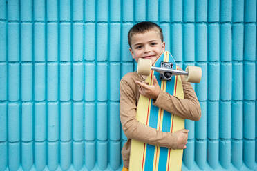 Smiling boy with skateboard in front of blue wall - RCPF01274
