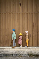 Children standing on footpath by brown wall - RCPF01277