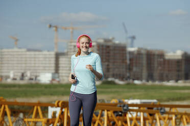 Smiling woman jogging at construction site - AANF00056