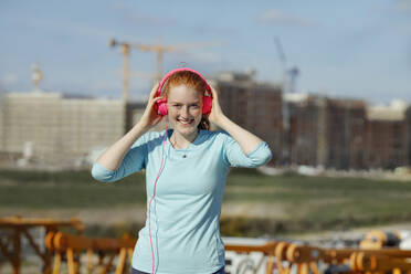 Young woman adjusting headphones at construction site - AANF00058