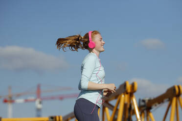 Smiling woman with headphones jogging during sunny day - AANF00079