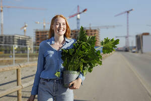Rothaarige Frau mit Pflanze, die auf einer Baustelle auf der Straße läuft - AANF00086
