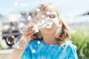 Girl blowing bubbles through wand on sunny day - OMIF00047