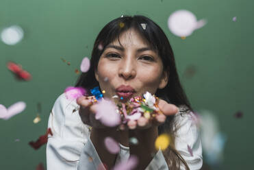Mittlere erwachsene Frau genießt beim Blasen von buntem Konfetti - DSIF00568