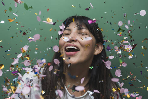 Happy woman with eyes closed amidst falling colorful confetti - DSIF00569