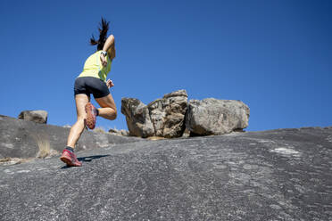 Weibliche Athletin, die an einem sonnigen Tag auf einen Felsenberg läuft - OCMF02217