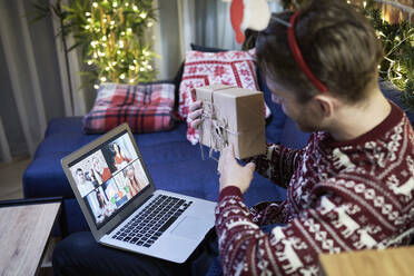 Mann zeigt Weihnachtsgeschenk bei Videoanruf über Laptop zu Hause - ABIF01617