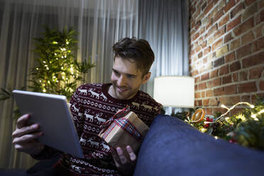 Man showing gift through digital tablet in living room - ABIF01625