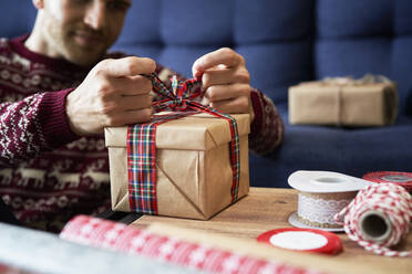 Mann bindet Schleife an Weihnachtsgeschenk zu Hause - ABIF01630