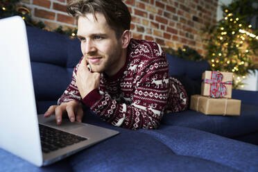 Young man using laptop while relaxing on sofa - ABIF01631