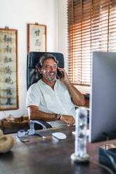 Smiling male freelancer talking on mobile phone at home - DLTSF02187