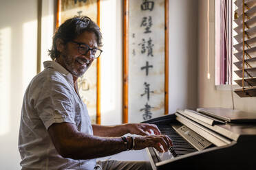 Smiling mature man playing piano at home - DLTSF02199