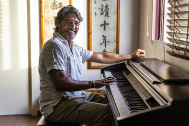 Smiling man playing piano at home - DLTSF02200