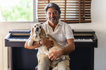 Mann sitzt mit Hund vor einem Klavier zu Hause - DLTSF02206