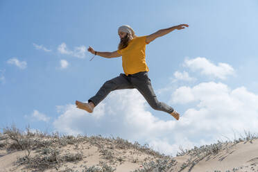 Carefree man with arms outstretched jumping on sand at beach - AFVF09184