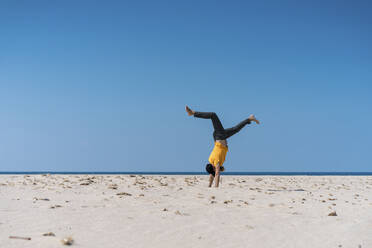 Man doing handstand on beach during sunny day - AFVF09188