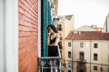 Sad woman with hand on chin standing at balcony - MRRF01516