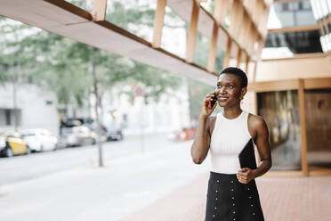 Smiling businesswoman holding digital tablet while talking on smart phone - JCZF00833