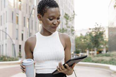 Geschäftsfrau hält Einwegbecher und liest auf einem digitalen Tablet - JCZF00835
