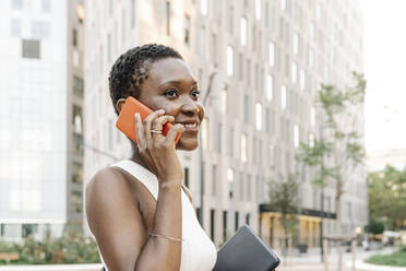 Smiling businesswoman with digital tablet talking on smart phone in city - JCZF00836