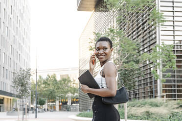 Smiling female freelancer talking on mobile phone in city - JCZF00839