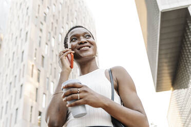 Lächelnde Geschäftsfrau mit Einwegbecher im Gespräch mit einem Smartphone - JCZF00843