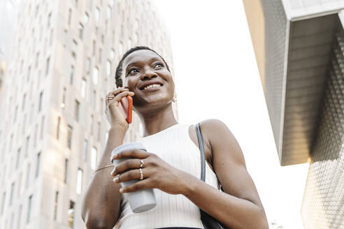 Smiling businesswoman with disposable cup talking on smart phone - JCZF00843