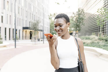 Businesswoman sending voicemail through mobile phone while standing on footpath - JCZF00848