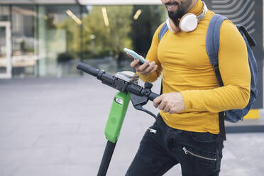 Mann mit Rucksack, der über sein Mobiltelefon einen Elektroroller mietet - JCCMF03881