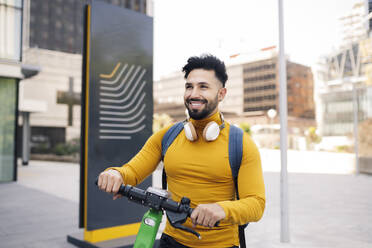 Lächelnder Mann mit Elektro-Scooter in der Stadt - JCCMF03882