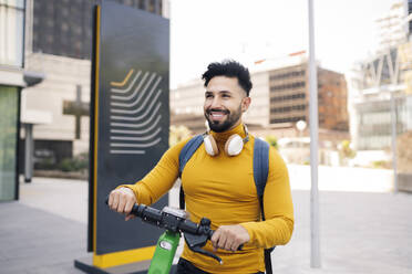 Smiling man with electric push scooter in city - JCCMF03882