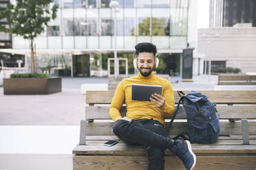 Man watching video through digital tablet while sitting on bench - JCCMF03883