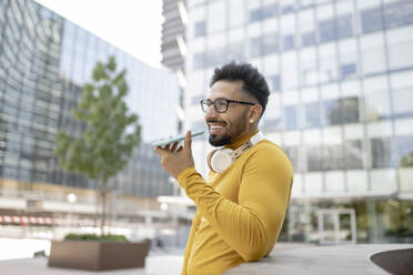 Mann mit Brille sendet in der Stadt Sprachnachrichten über sein Smartphone - JCCMF03887