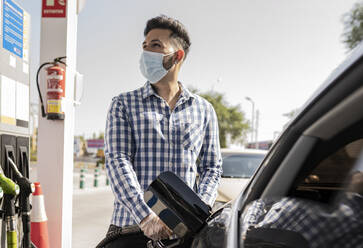 Mann mit Gesichtsmaske tankt an einer Tankstelle Benzin ins Auto - JCCMF03903