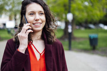 Lächelnde Frau, die im Park mit einem Mobiltelefon spricht - AMWF00001